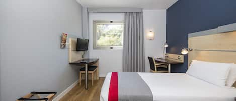 A hotel room with a bed, desk, chair, and a window with curtains.