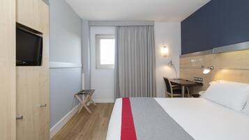 Habitación de hotel con cama, escritorio, silla, televisor y ventana con cortinas.