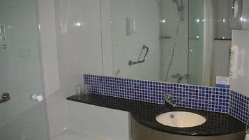 Une salle de bain avec un lavabo blanc, une cabine de douche en verre et un mur recouvert de carreaux bleus derrière le lavabo.