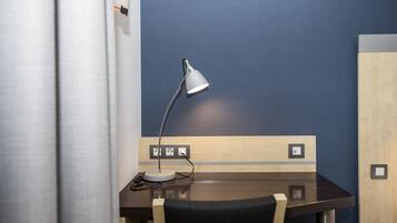 A hotel room with a wooden desk, a desk lamp, and a power outlet.