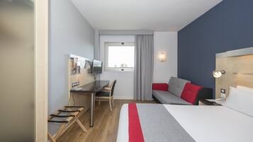 Habitación de hotel con cama, escritorio, silla, televisor y ventana con cortinas.