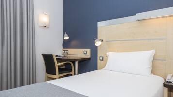 Habitación de hotel con cama, escritorio, silla y dos lámparas de pared.