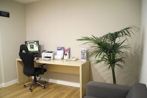 A reception desk with a computer, printer, and phone, a black office chair, a grey sofa, and a potted plant. - Holiday Inn Express Barcelona-Montmeló by IHG (Granollers)