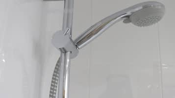 A chrome showerhead with a handheld attachment, mounted on a wall with white tiles.