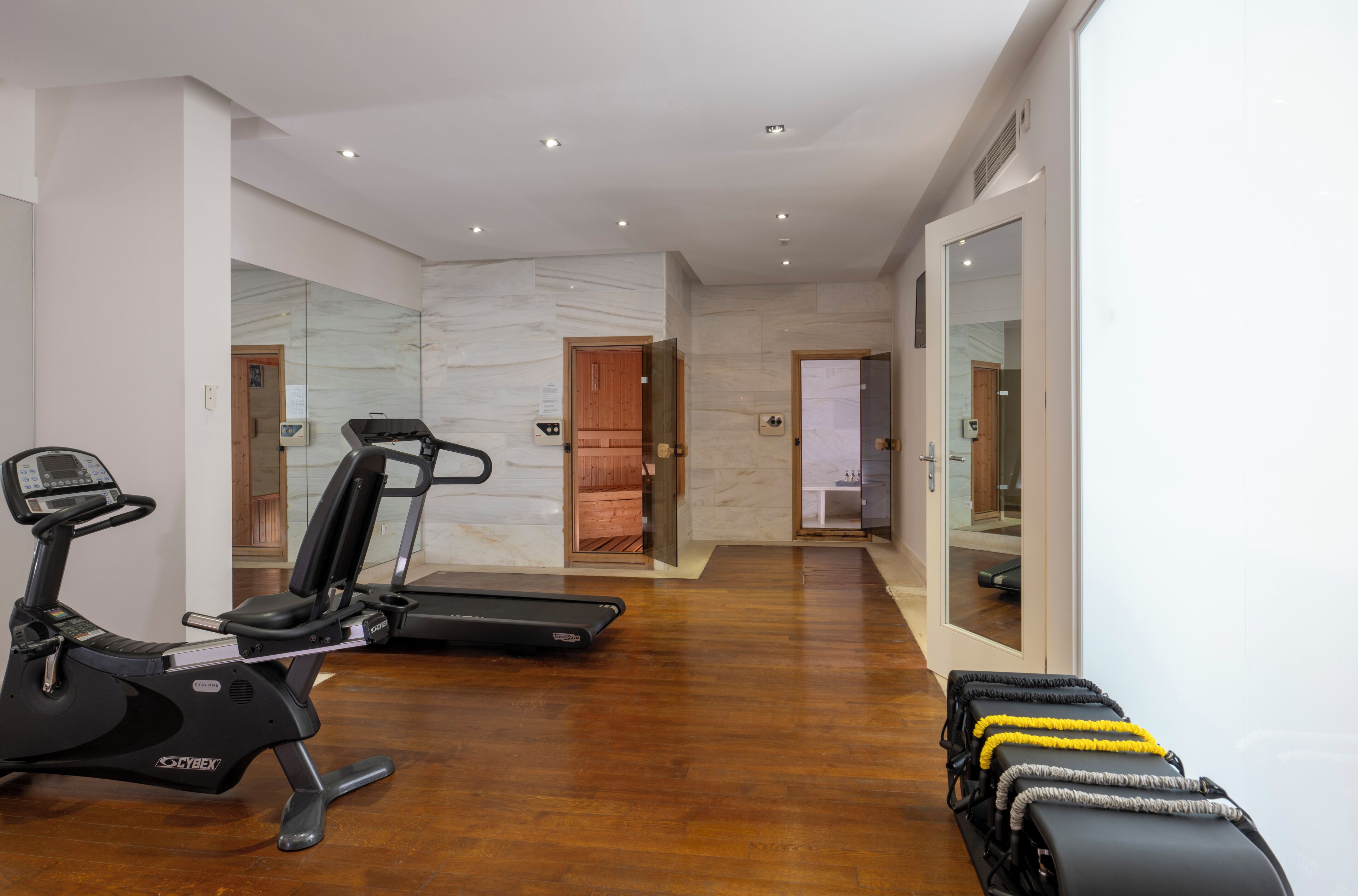 Un gimnasio moderno con equipo de ejercicio, piso de madera y puerta de cristal que da a otra habitación.