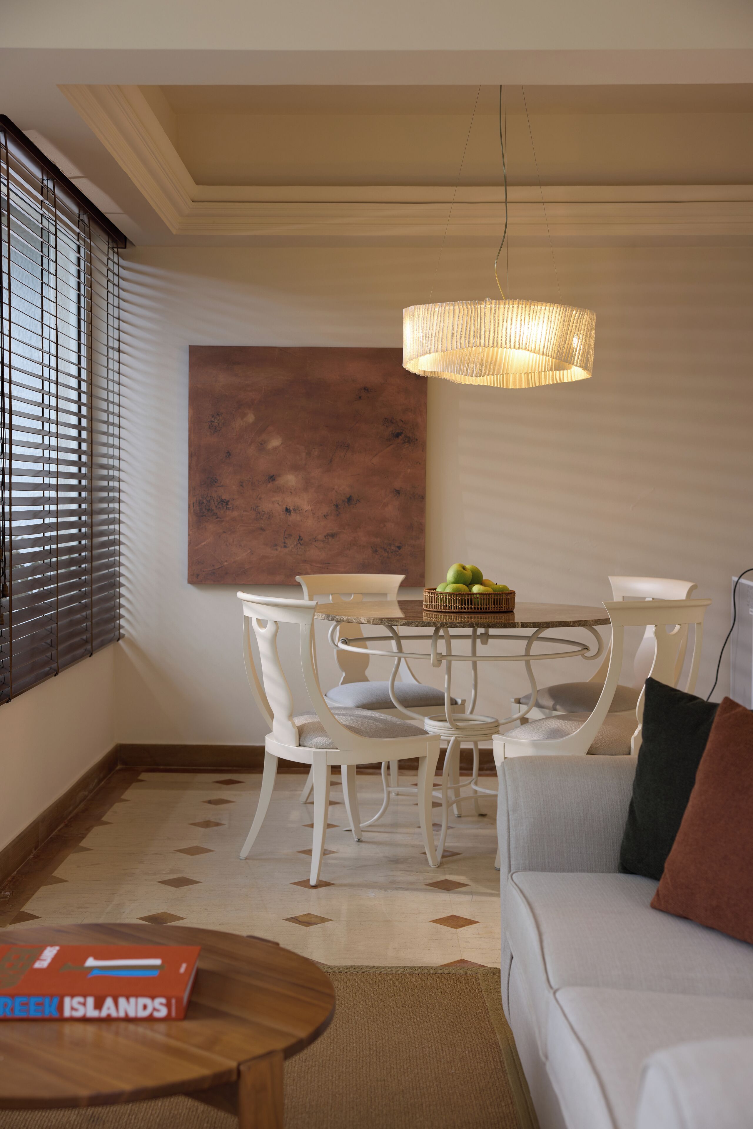 A modern dining area with a round table, white chairs, and a hanging light fixture.