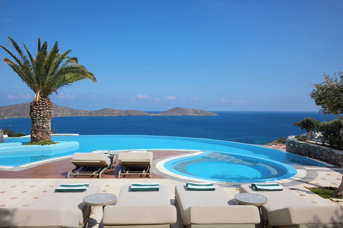 A pool area with lounge chairs and a palm tree, overlooking the sea.