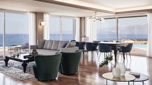 A spacious living room with a large window overlooking the sea, a cozy seating area, and a dining setup.