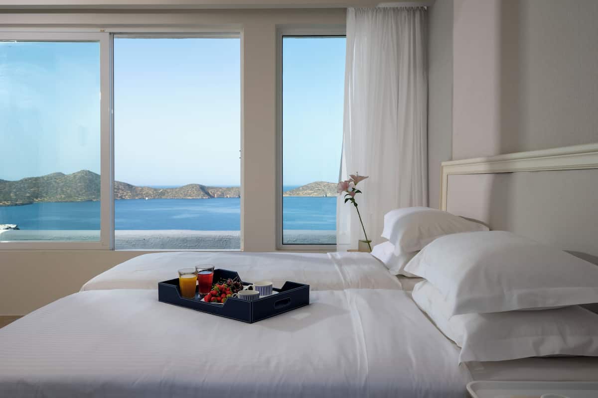 A hotel room with a large bed, a tray of breakfast items, and a view of the sea.