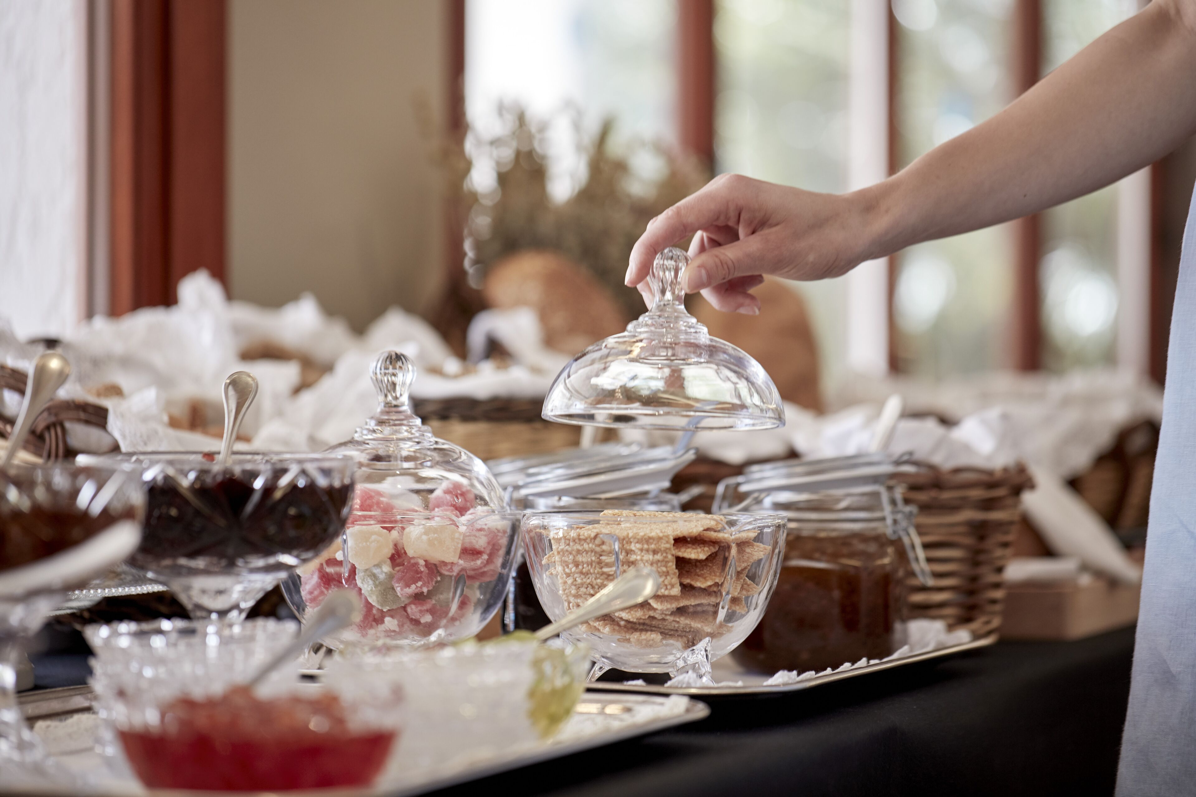 Une table de buffet garnie de divers plats, et une main qui tend vers un récipient en verre.