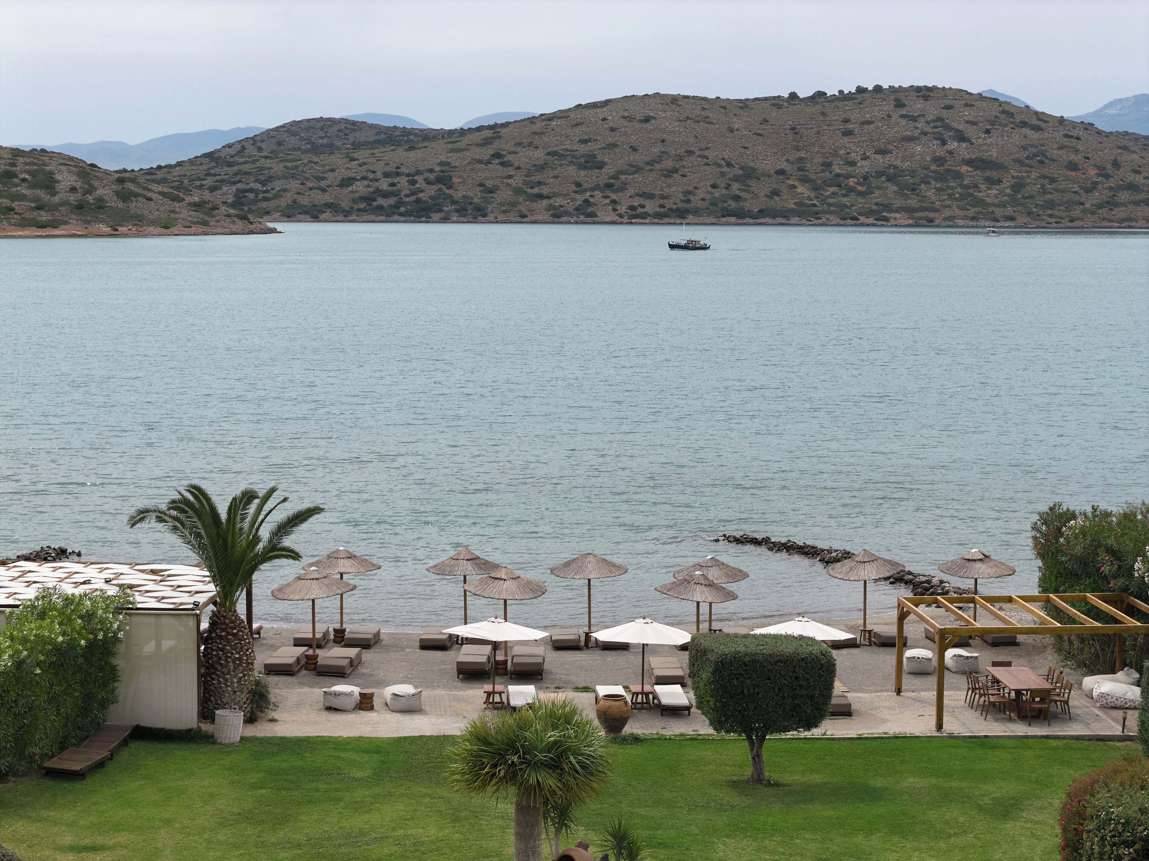 Une vue sur la côte, avec un bateau sur l’eau, une terrasse avec des parasols et une montagne en arrière-plan.