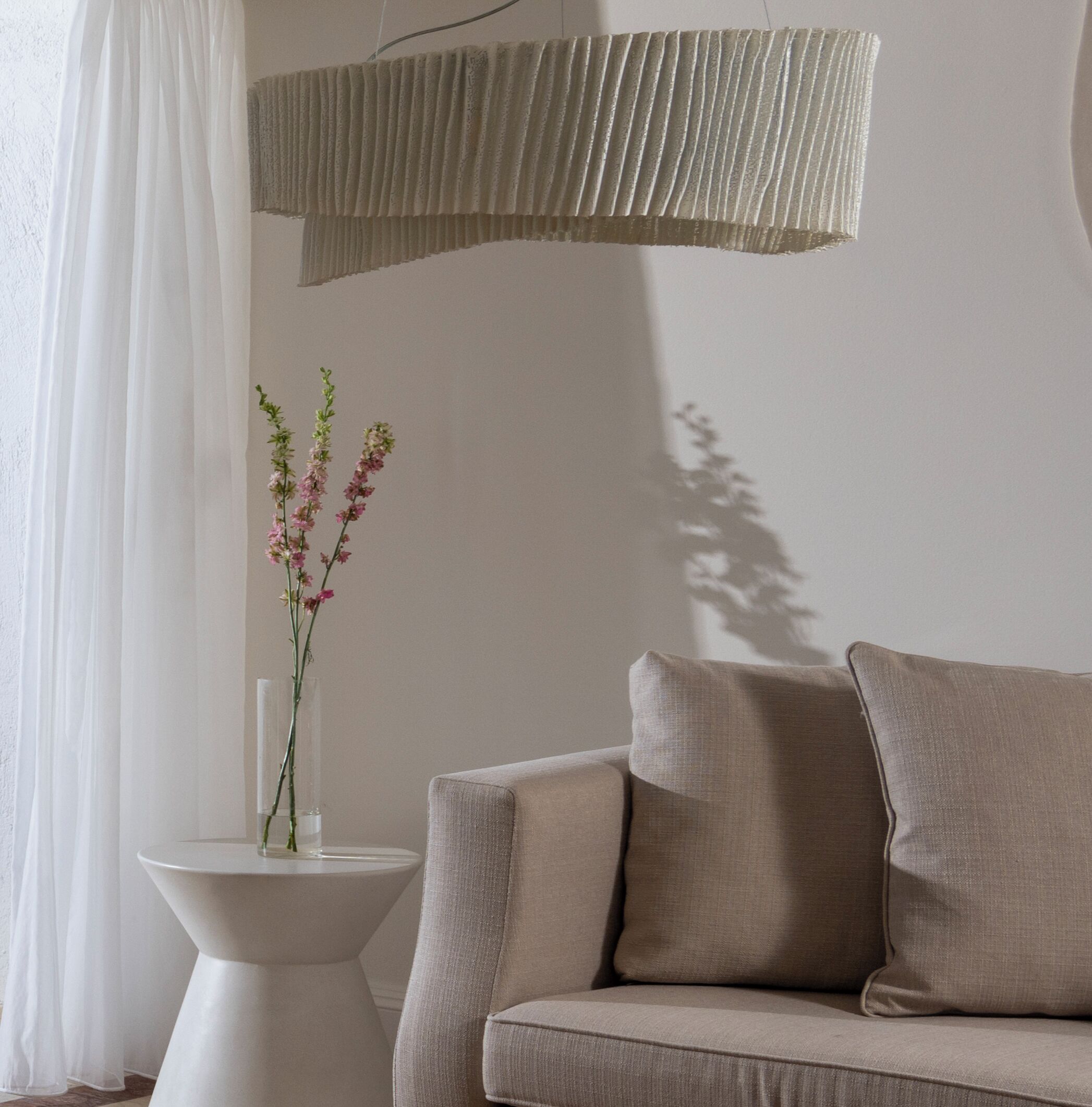 A modern living room with a beige sofa, a white side table, and a vase with flowers.