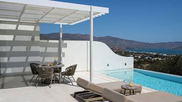 A modern outdoor pool area with a white wall, lounge chairs, and a dining table.