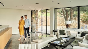 A modern interior with a glass wall, a sofa, a coffee table, and a stone wall visible through the glass.