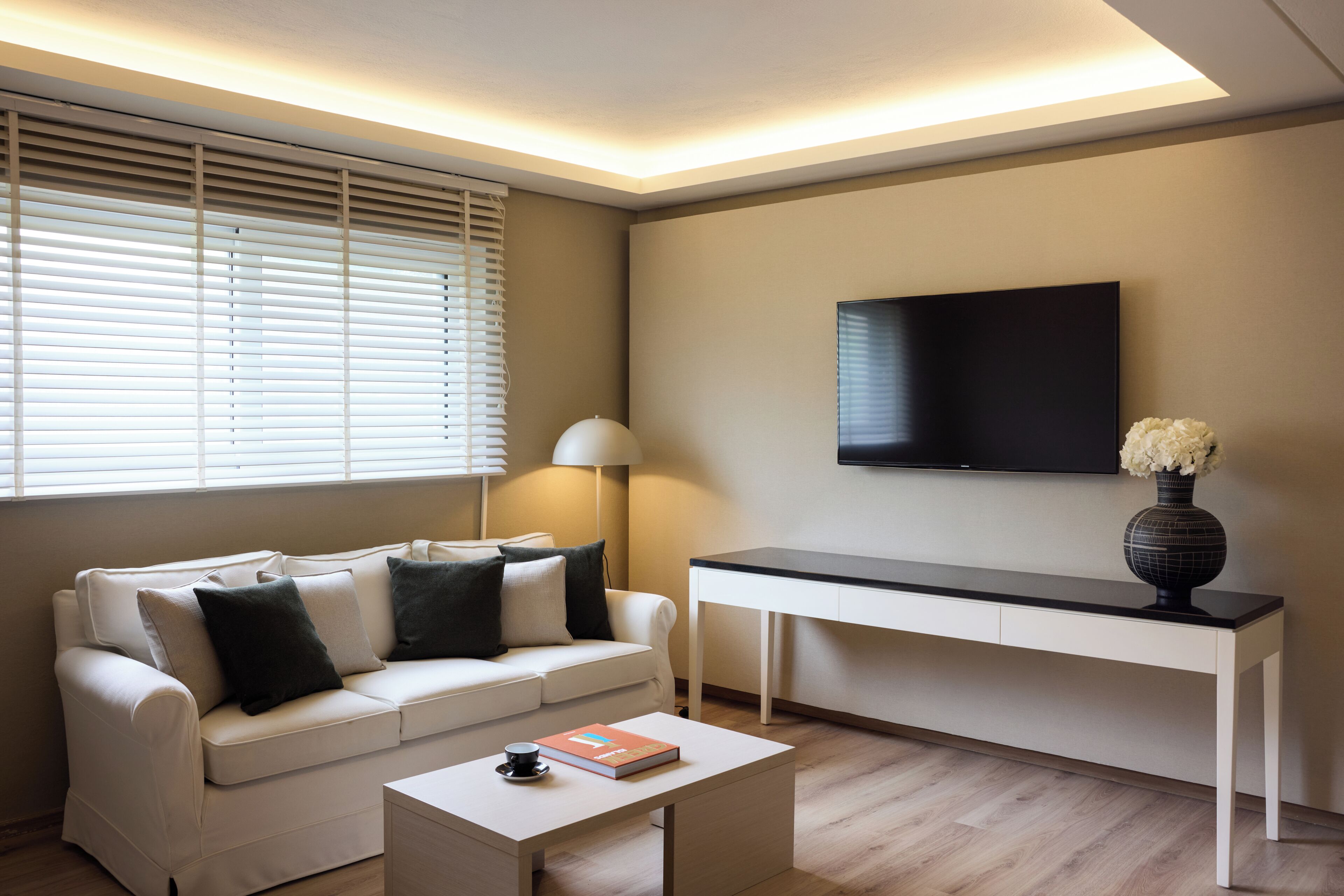 Una sala de estar moderna con sofá, mesa de centro, escritorio y un televisor de pantalla plana montado en la pared.