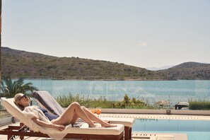 A person relaxing on a sun lounger by a pool with a view of a lake and hills. - Elounda Gulf Villas by Sandglass (Agios Nikolaos)