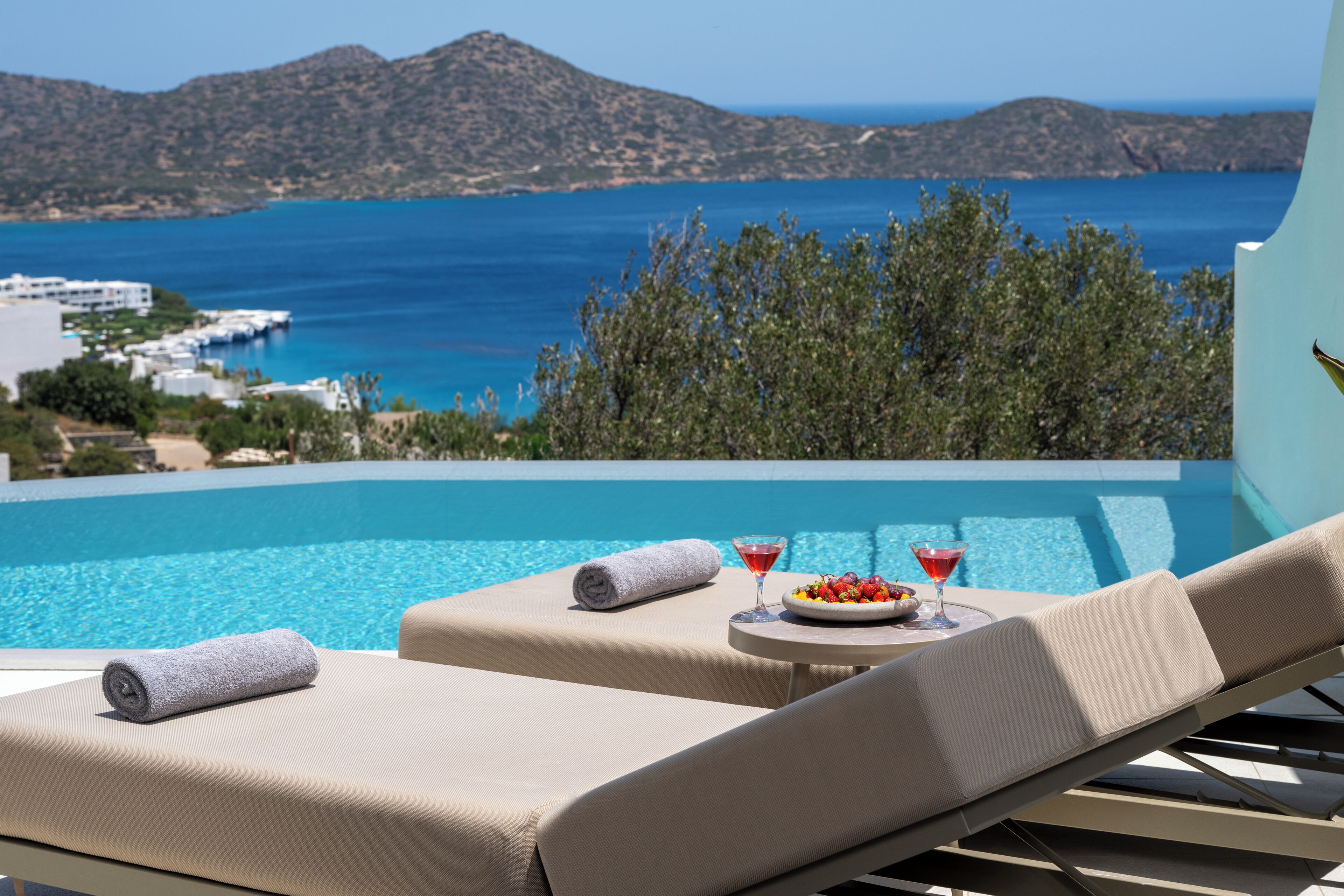 A poolside lounge with a view of the sea and mountains.