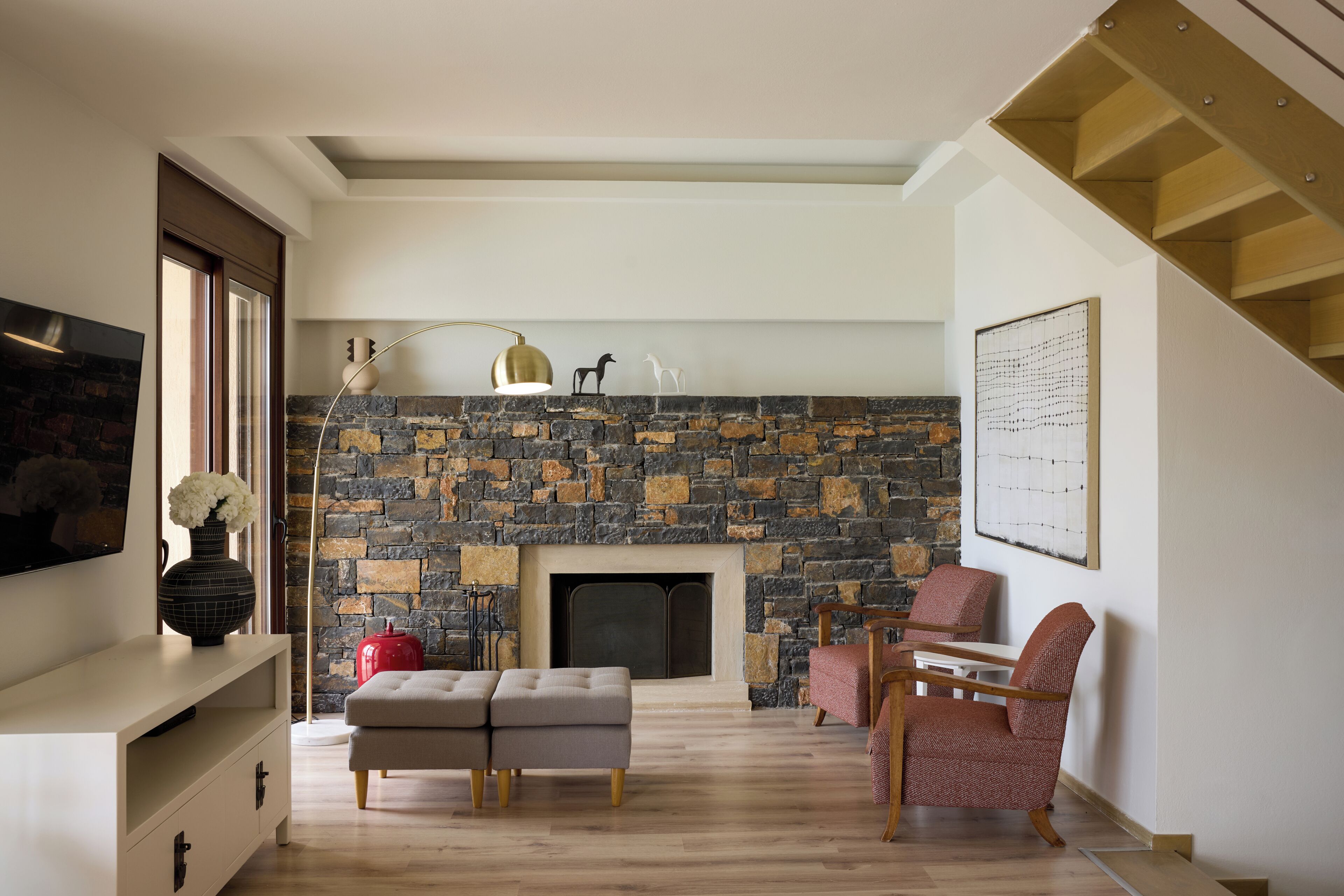 A living room with a stone fireplace, a sofa, a chair, a TV, and a staircase.