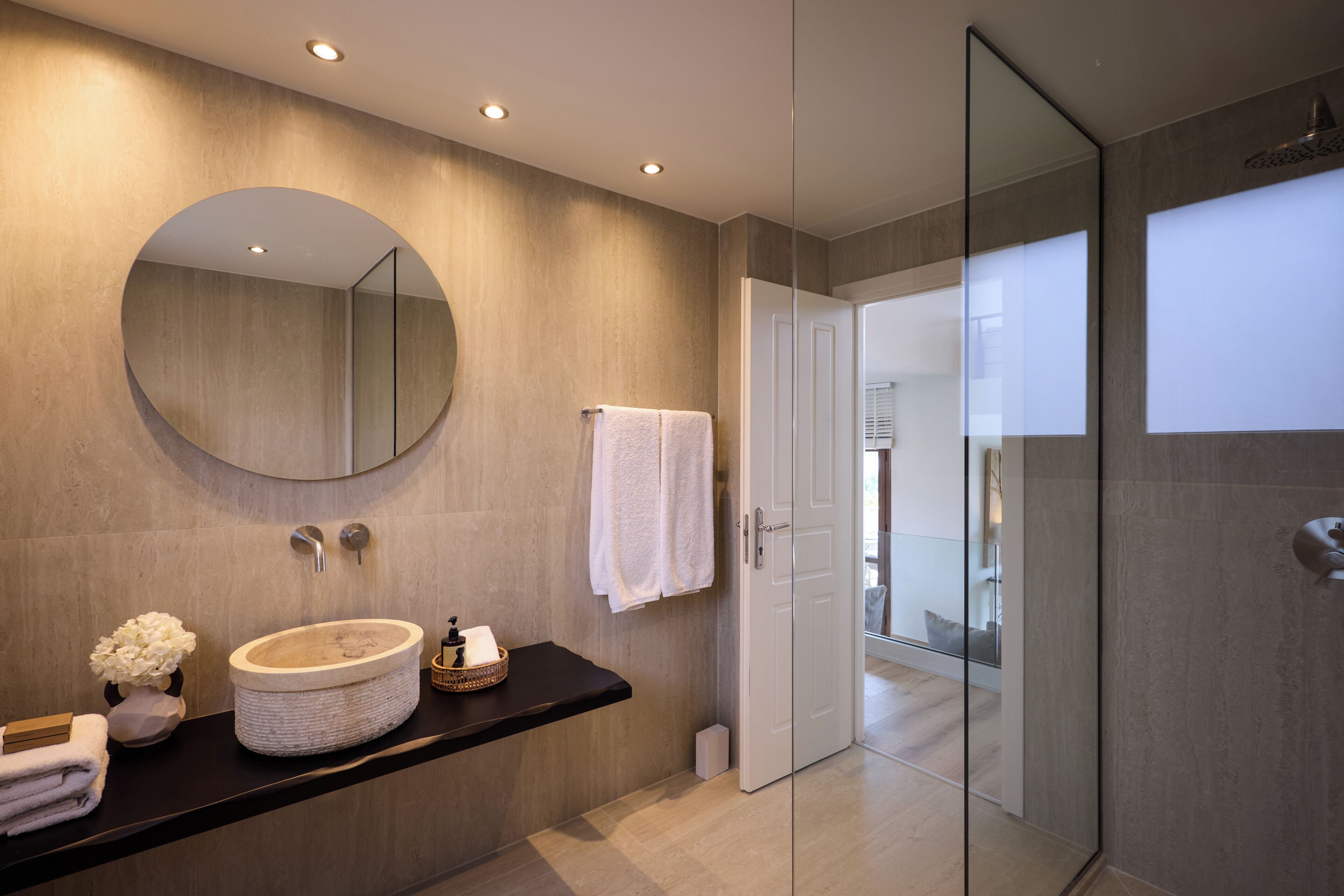 A modern bathroom with a round mirror, a sink with a large basin, a towel rack, and a glass shower enclosure.