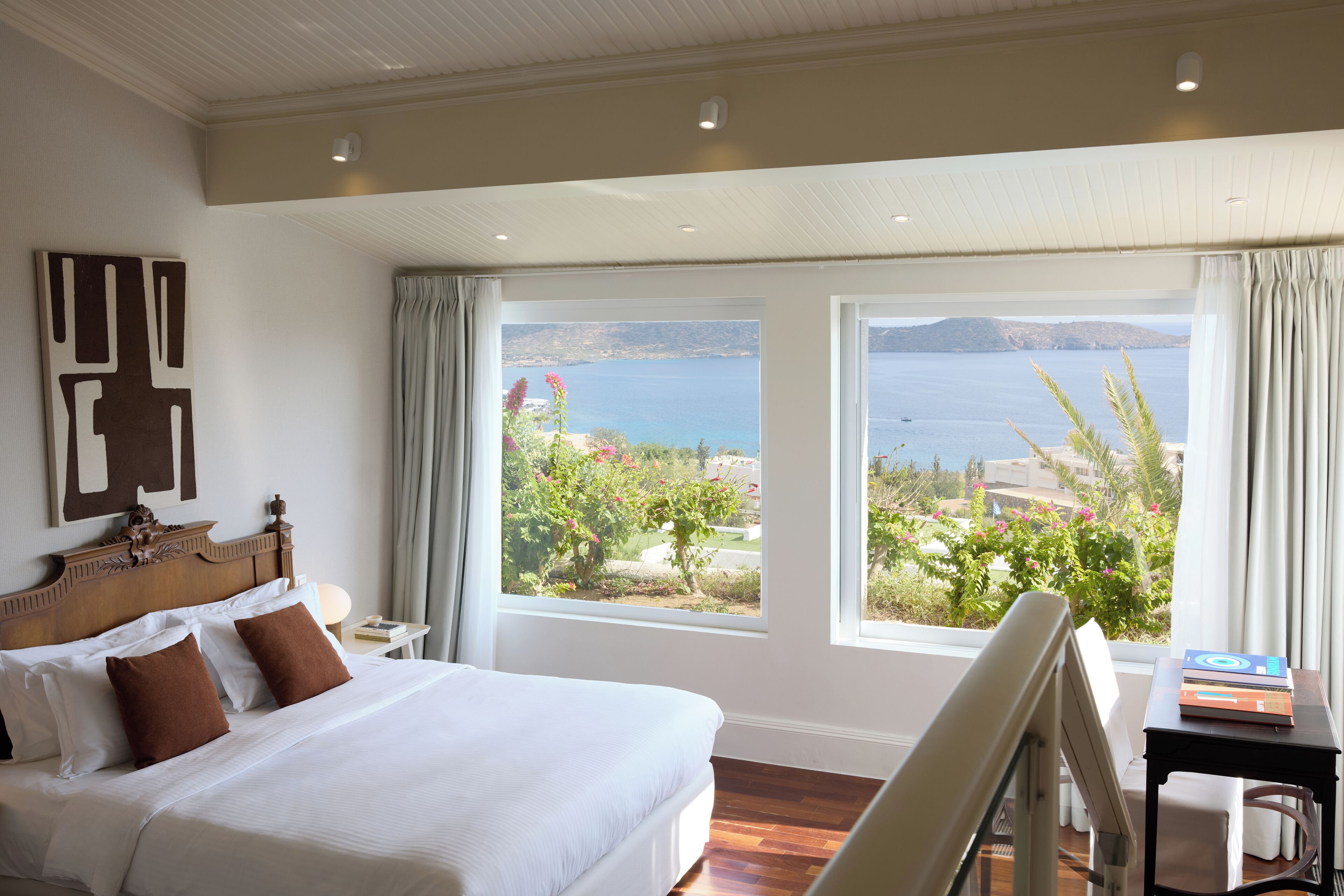 Une chambre avec un grand lit, une vue sur la mer et une table avec des livres.