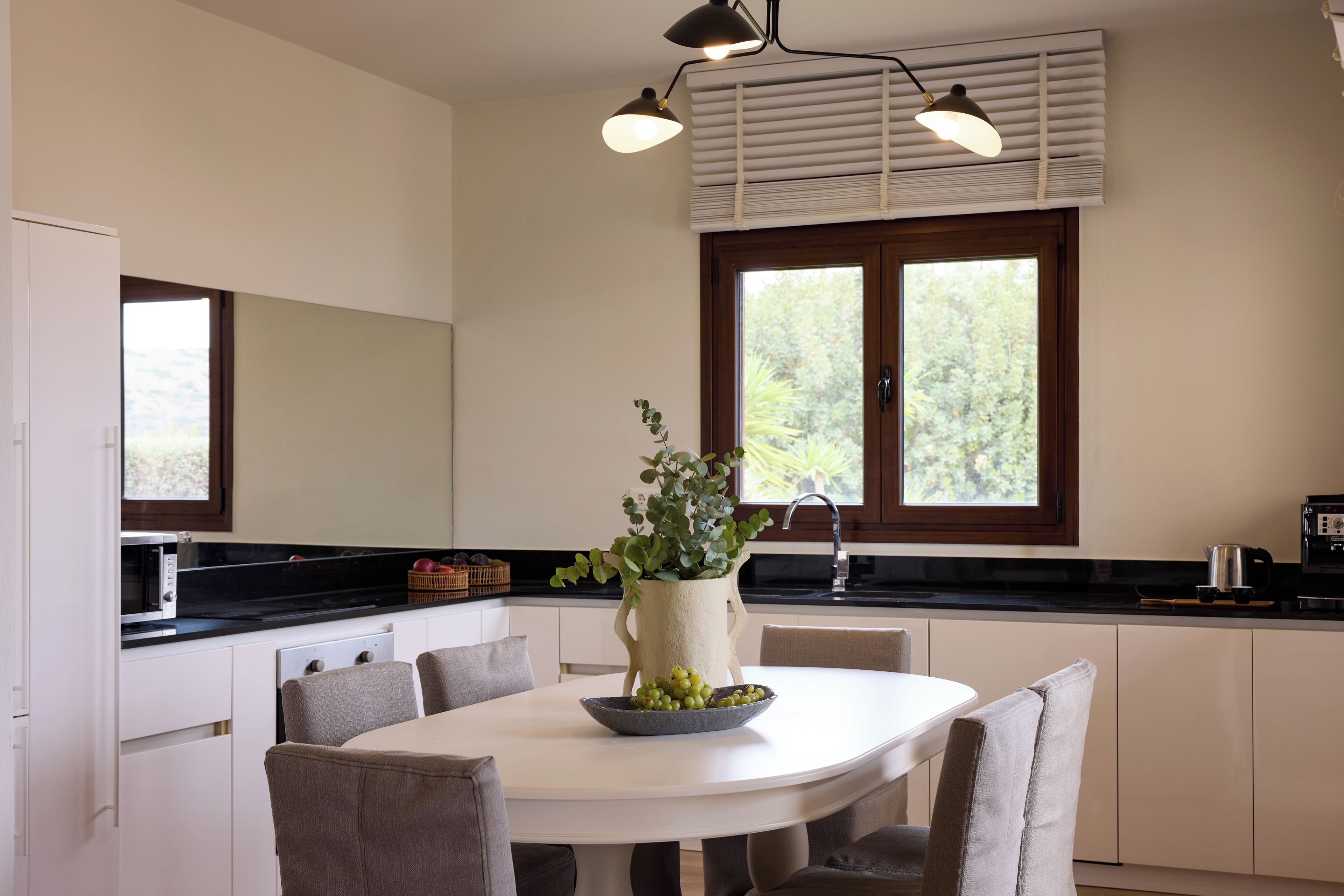 Une cuisine moderne avec une table à manger blanche, des chaises, une plante en pot et une grande fenêtre.