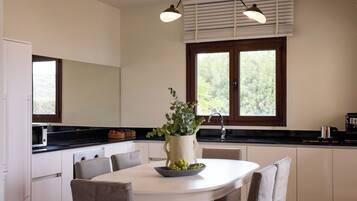 A modern kitchen with a white dining table, chairs, a potted plant, and a large window.