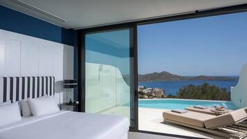 A modern bedroom with a large bed, a bedside table, a lamp, and a view of a pool and landscape.