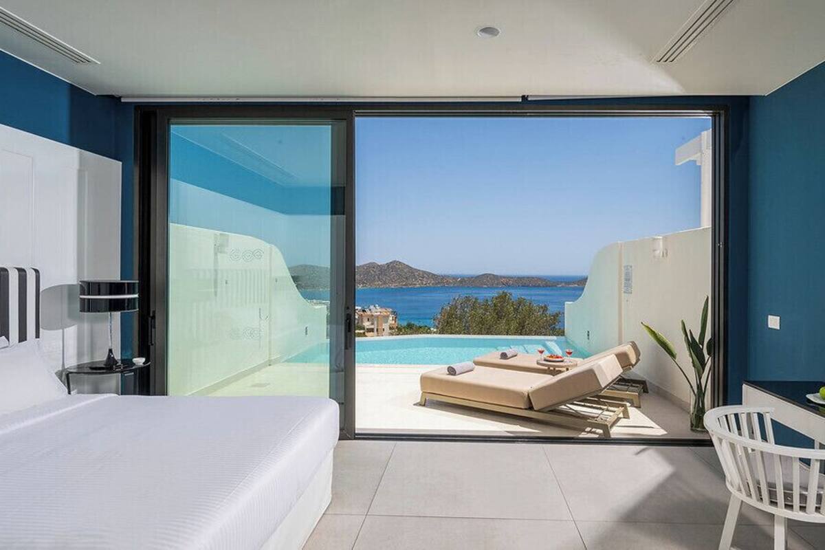 Una habitación de hotel moderna con una cama grande, un escritorio, una silla, un televisor y un balcón con vistas al mar.