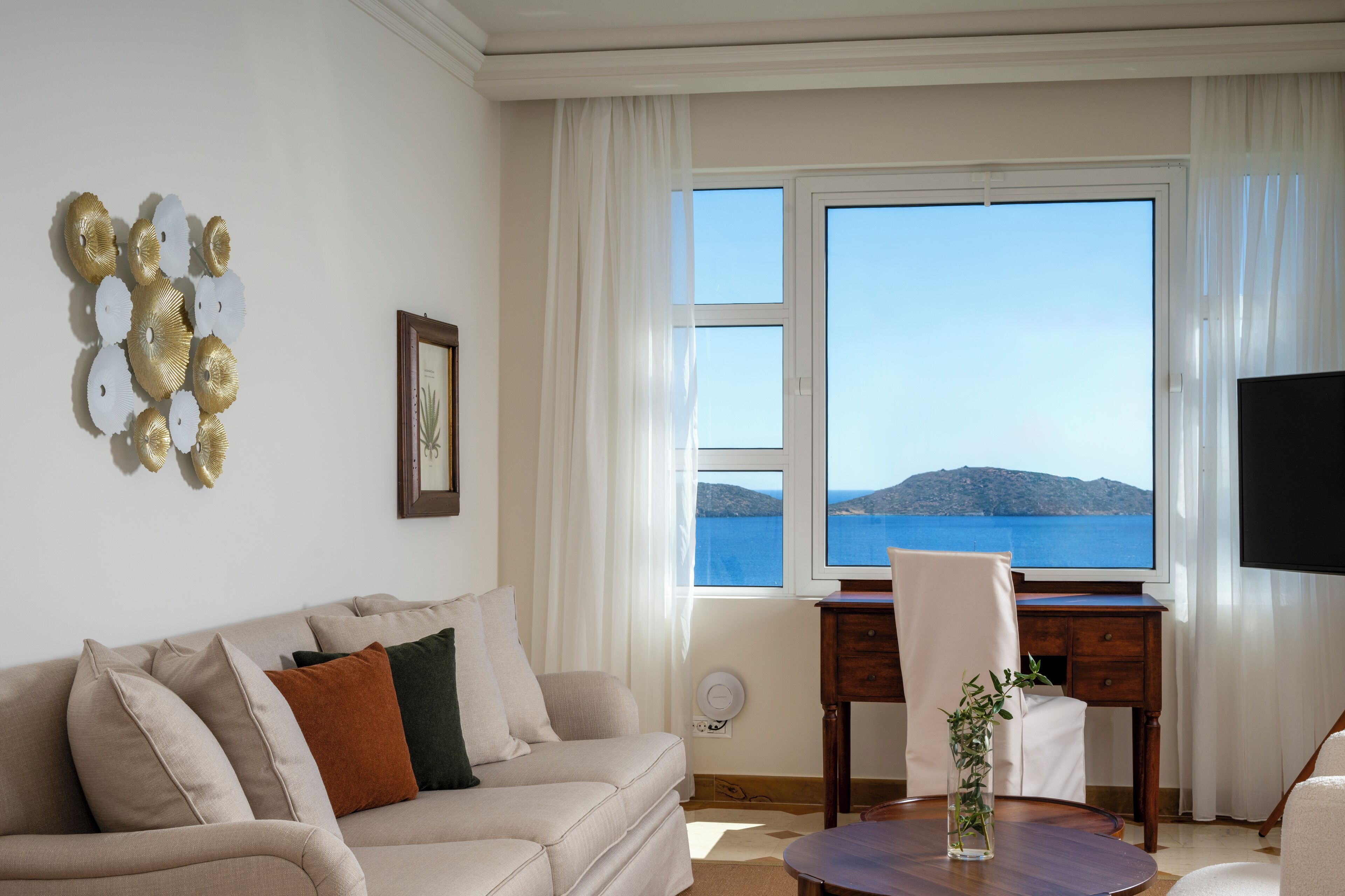 Ett vardagsrum med en soffa, ett soffbord, en tv och utsikt över havet.