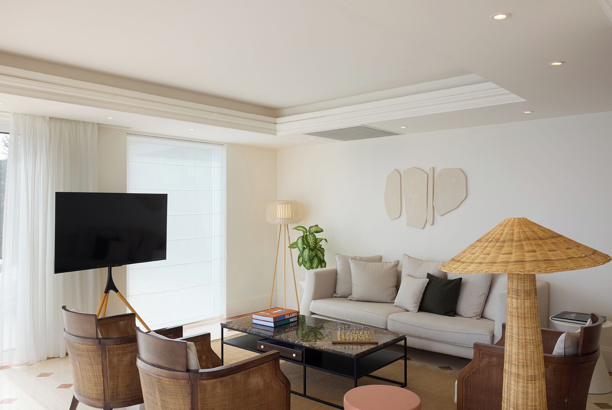 A modern living room with a sofa, coffee table, and chairs. There is a TV on a stand, a lamp, and a bookshelf with books.