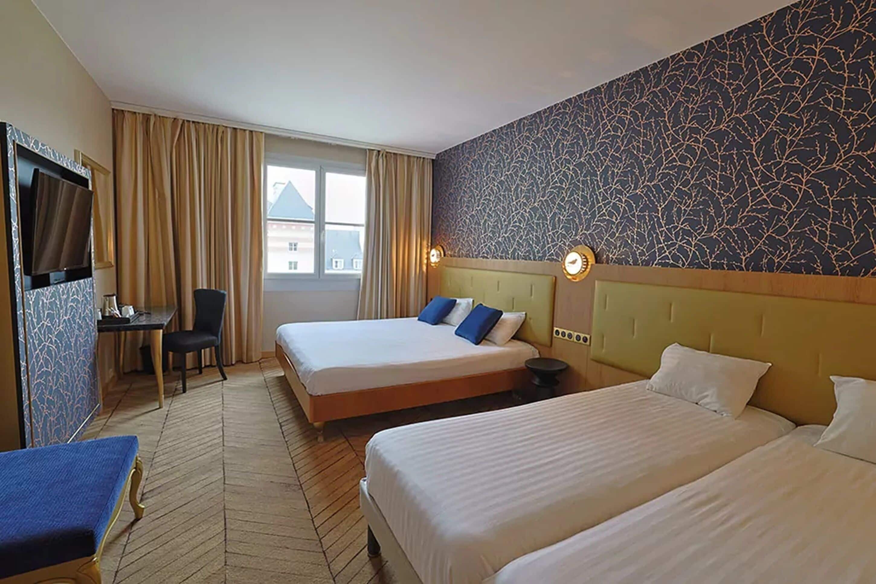 A hotel room with two beds, a desk, a chair, a TV, and a window with curtains.