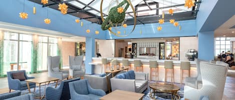 A spacious lobby with seating areas, a bar, and a large glass ceiling with hanging decorations.