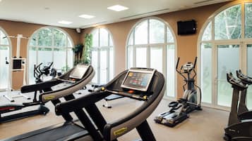 A gym with treadmills, stationary bikes, and a TV screen.