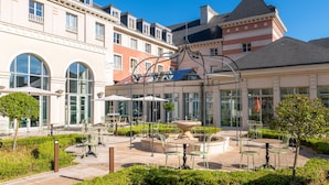 A courtyard with outdoor seating, a fountain, and a building with multiple floors and large windows.