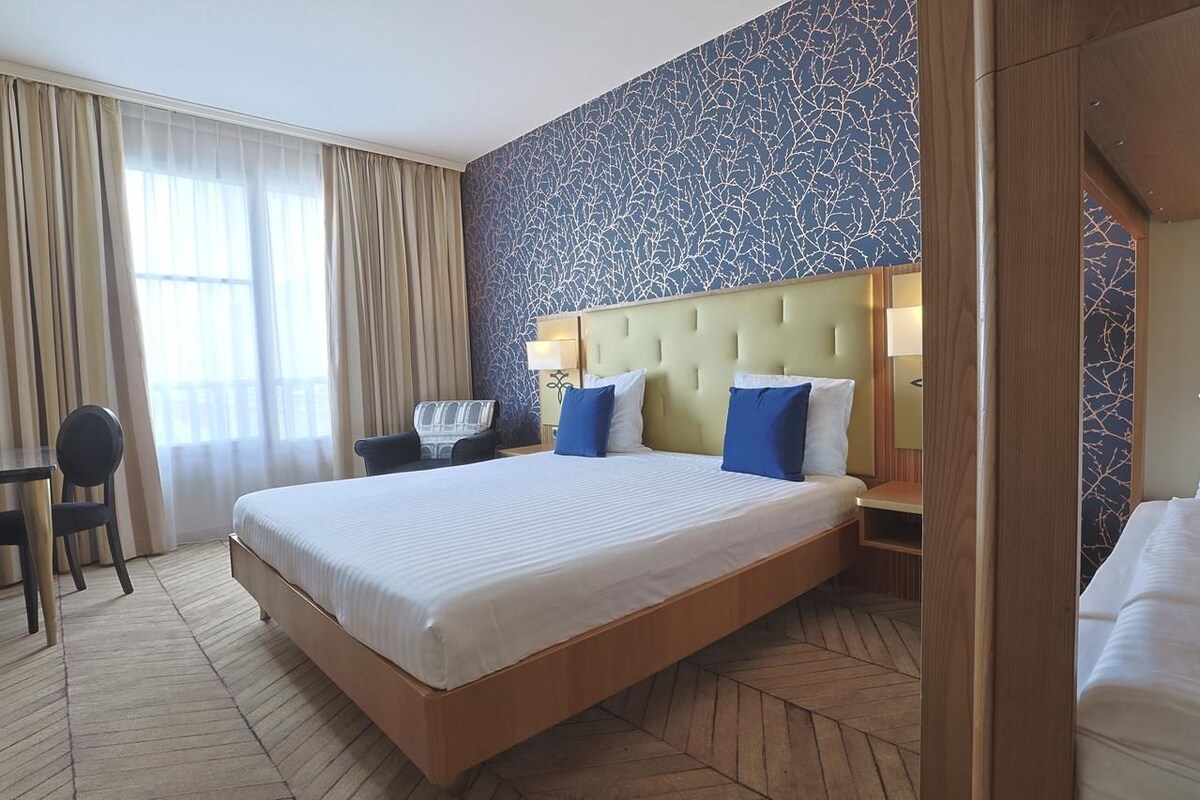 A hotel room with a large bed, a desk with a chair, and a window with curtains.