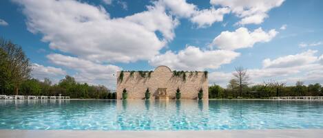 Una piscina con un muro de piedra y follaje al fondo.