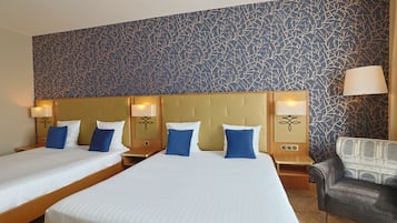 Een hotelkamer met twee bedden, een bank en een behang met patroon.