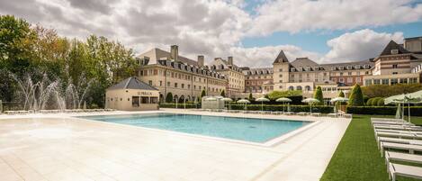 A hotel courtyard with a swimming pool, lounge chairs, and a fountain.