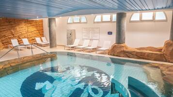 Una piscina interior con una fuente de agua cristalina, sillas de descanso y una pared de piedra.