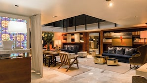 A spacious living area with a high ceiling, a dining table with chairs, a sofa, a bookshelf, and a large window with stained glass. - Hotel Matilda, a Member of Design Hotels (San Miguel de Allende)