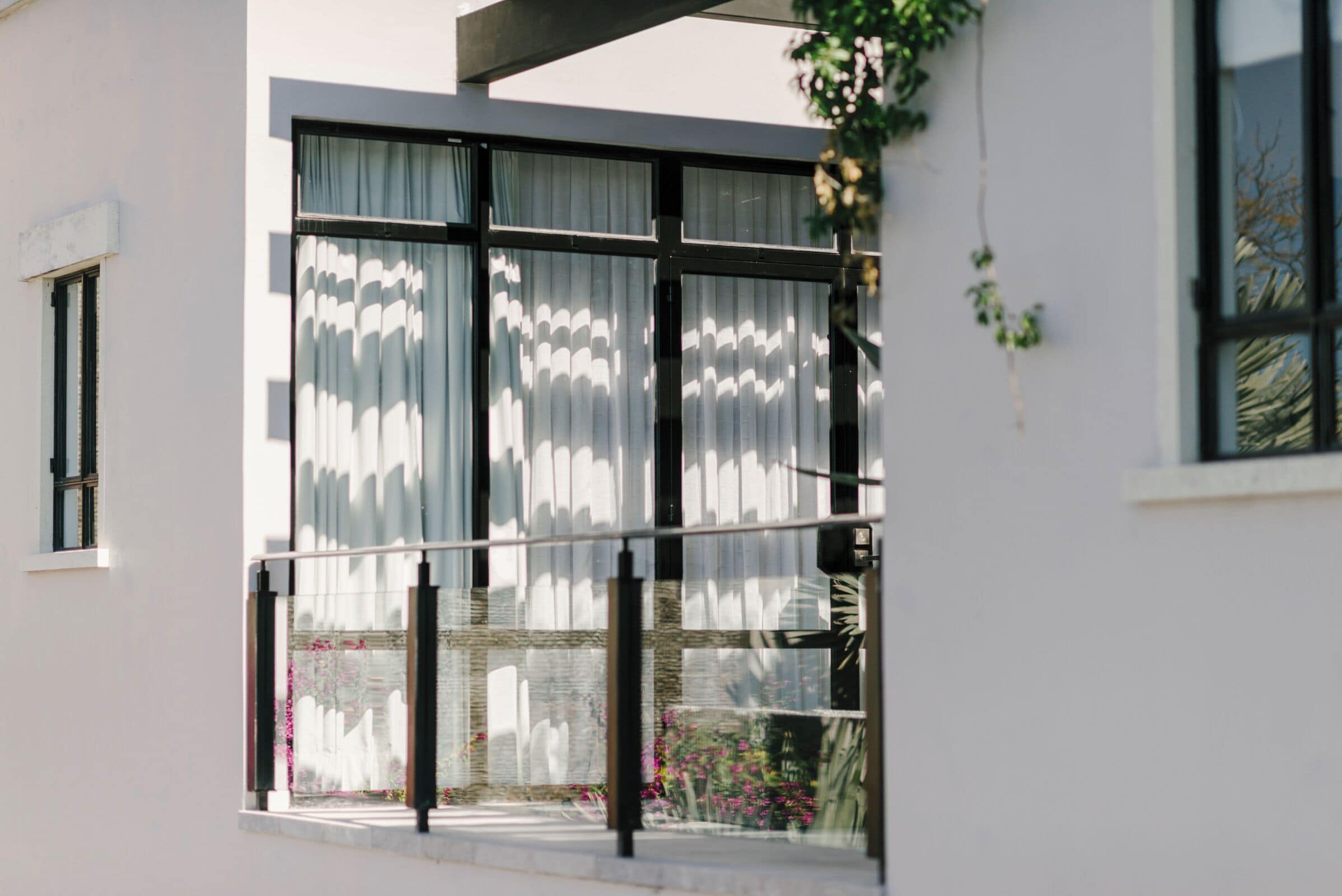 Un edificio moderno con grandes ventanales, un balcón y vistas a flores rosadas.