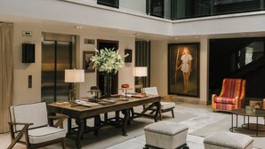 A spacious hotel lobby with a high ceiling, a central seating area with a table and chairs, a large painting on the wall, and a staircase leading to an upper level. - Hotel Matilda, a Member of Design Hotels (San Miguel de Allende)