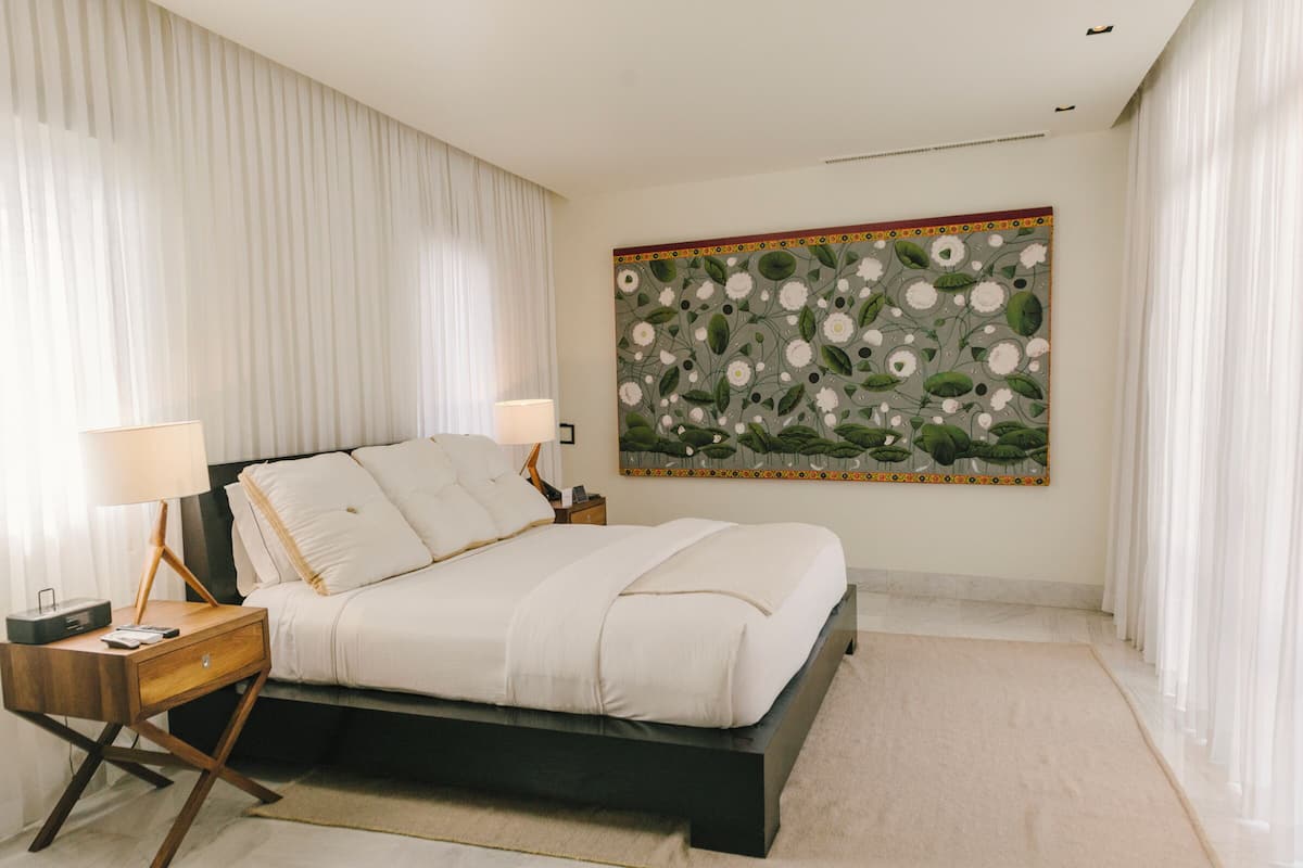 A bedroom with a bed, nightstands, a lamp, and a large floral painting on the wall.