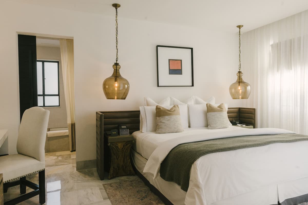 A hotel room with a large bed, two bedside tables, a chair, and a framed picture on the wall.