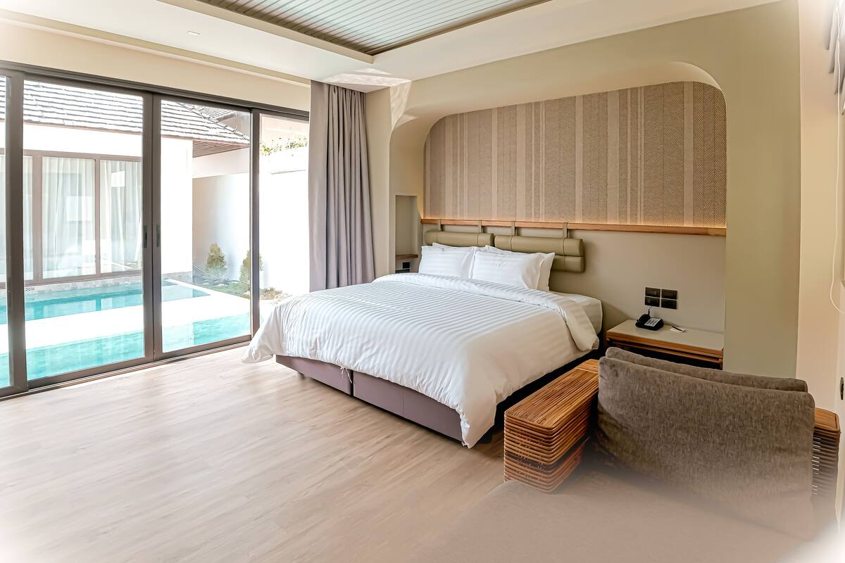 A modern hotel room with a large bed, a bedside table, a nightstand, a large window, and a view of a swimming pool.