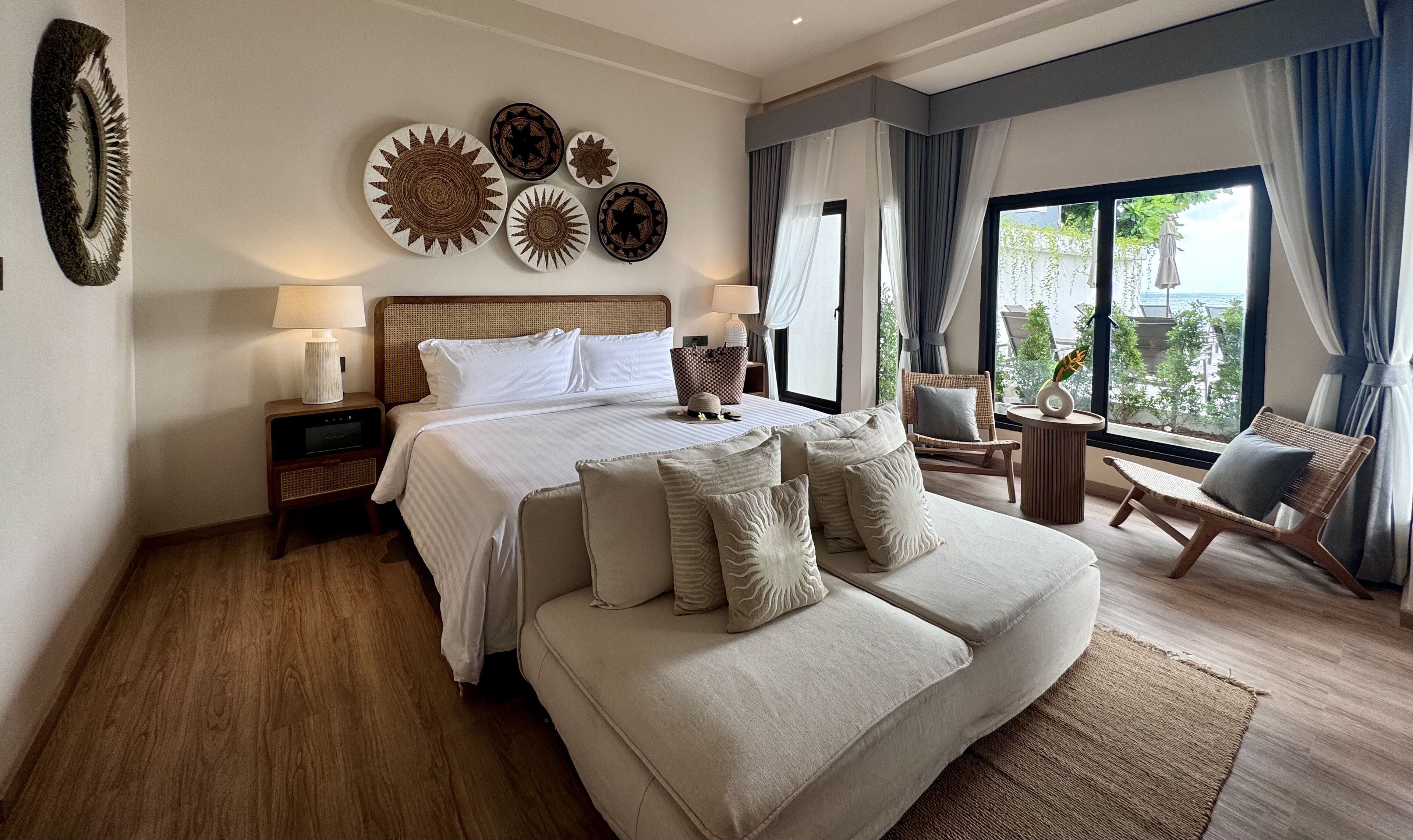 Een hotelkamer met een bed, een bank, een bijzettafeltje, een lamp en uitzicht op het omliggende landschap.