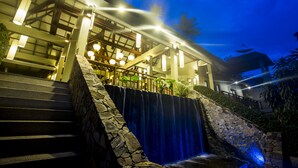 A hotel with a stone staircase leading to a waterfall, modern architecture, and outdoor lighting. - Baan Haad Ngam Boutique Resort & Villas (Koh Samui)