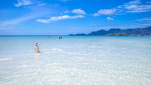 A beach with clear water and a woman sitting on the sand. - Baan Haad Ngam Boutique Resort & Villas (Koh Samui)