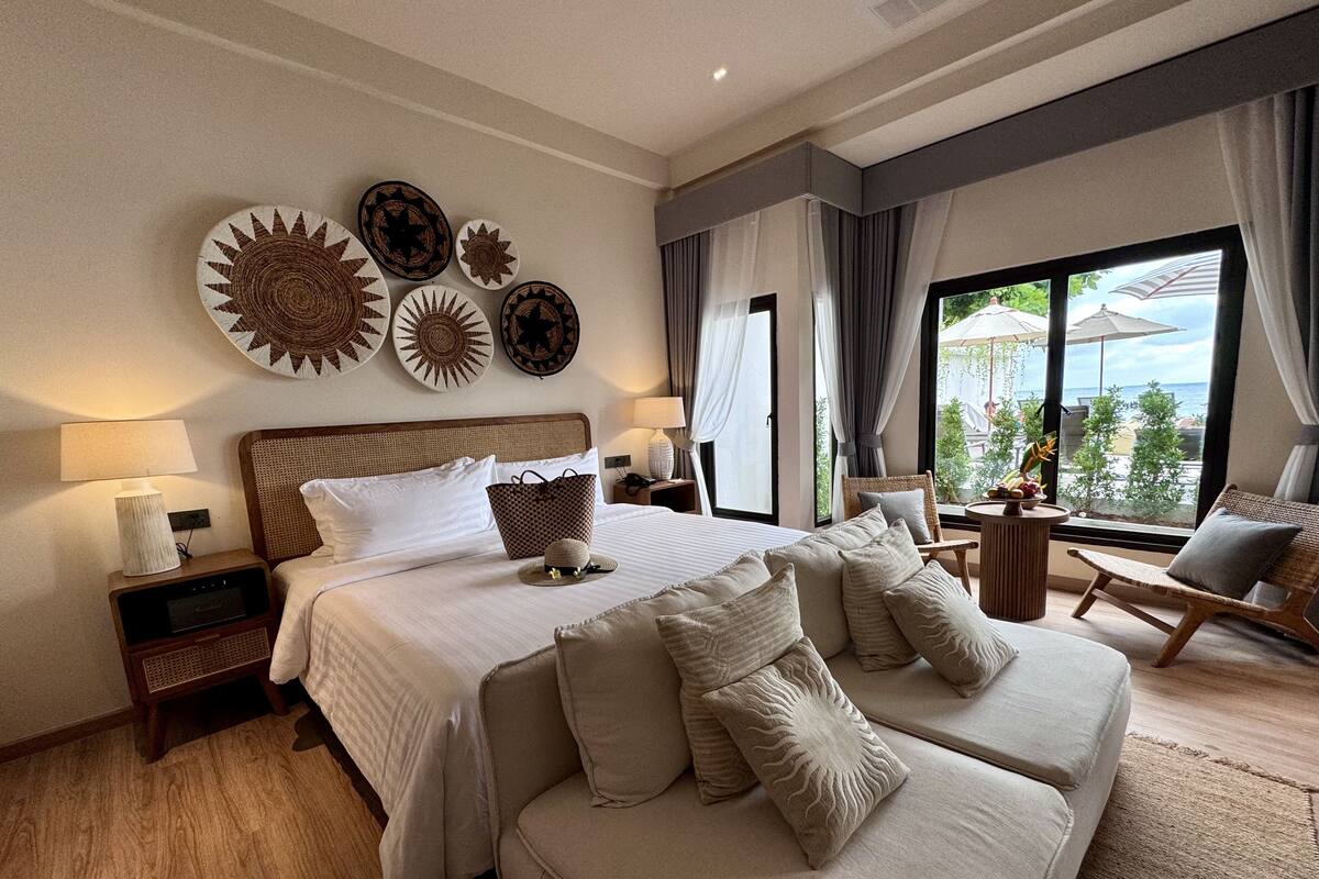 A hotel room with a large bed, two sofas, a small table, and a view of the outdoors.
