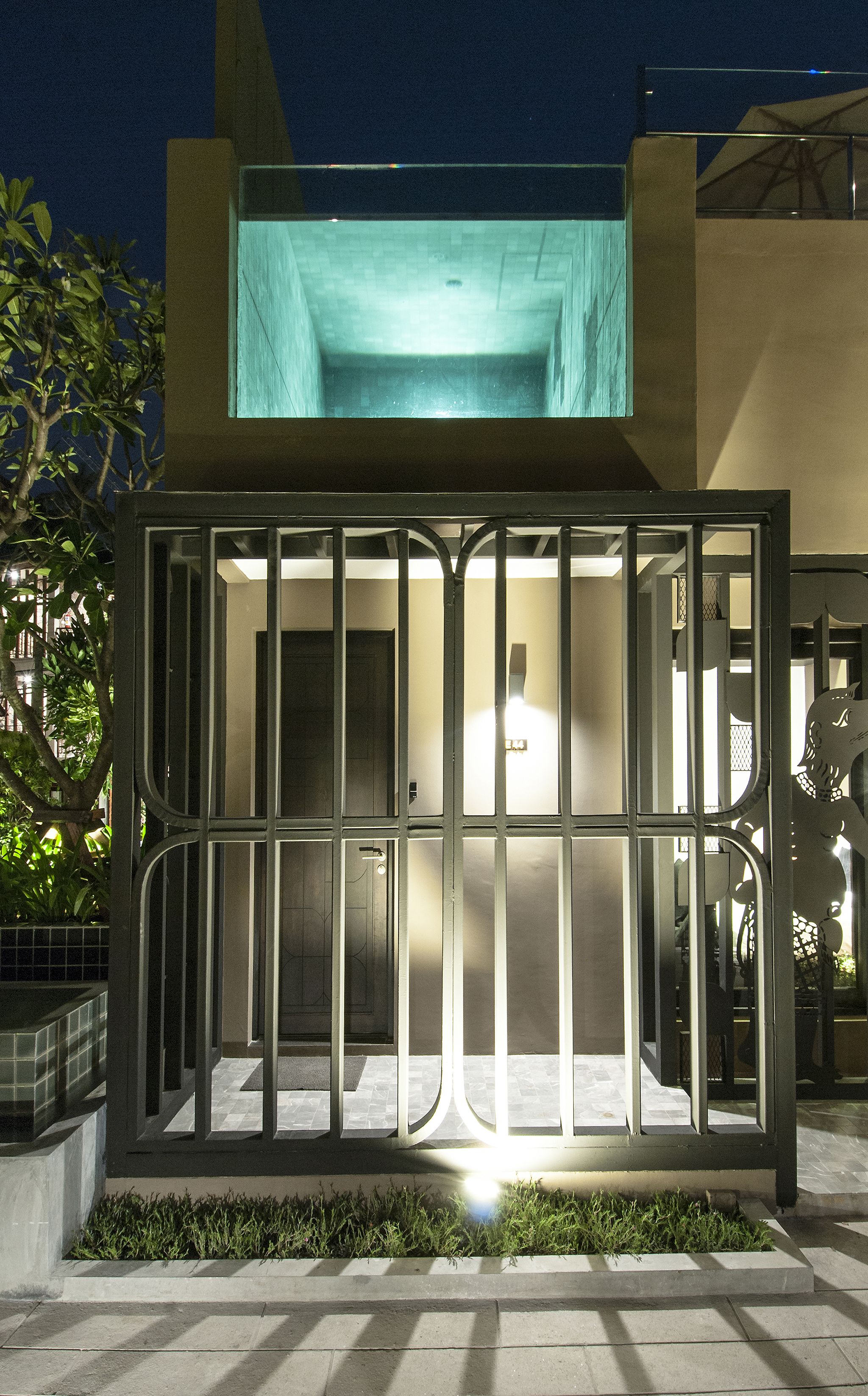 A modern building with a glass facade, metal railings, and a small garden area in front.